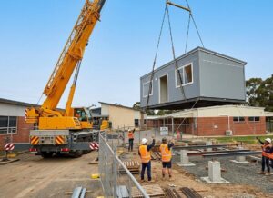 mobile crane lifting a prefab classroom module into position on a school site