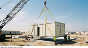 Crane placing a laundry cabin for labour camps onto a concrete foundation during site installation